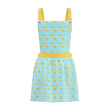 A light blue apron-style dress with a yellow duck print, featuring yellow shoulder straps, a yellow waistband, and silver metal snap buttons at the top, shown against a plain light gray background.