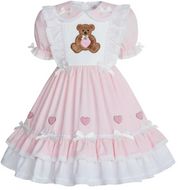 A pink and white adult baby girl's dress featuring a white bib front with an embroidered brown teddy bear holding a pink heart, short puff sleeves, and a tiered skirt decorated with pink hearts and white bows.