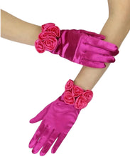 Bright pink satin opera gloves with 3D rose embellishments on the cuffs, shown worn on a model's hands and arms against a white background.