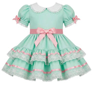 A mint green and pink adult toddler style girl's dress with a white Peter Pan collar, puffed sleeves with lace trim, a pink waistband with a large bow, and a tiered skirt with lace and satin ribbon details.