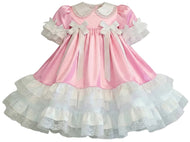 A pink and white adult baby girl's dress with a satin pink bodice, white ruffled collar and sleeves, and a tiered white ruffled skirt with lace trim.