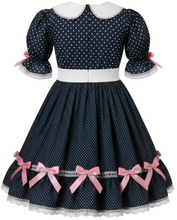 A navy blue and white polka dot dress displayed on a mannequin. The dress features a Peter Pan collar, short puff sleeves with pink ribbon accents at the cuffs, a white waistband, and a flared skirt decorated with pink bows and white lace trim.