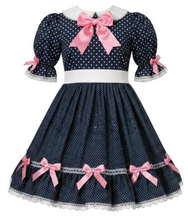 A navy blue and white polka dot dress with pink satin bows, a white collar, and puff sleeves, displayed on a mannequin against a white background.