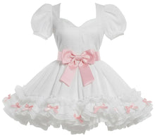 White baby girl's dress with puff sleeves, a sweetheart neckline, a large pink ribbon bow at the waist, and a layered ruffled skirt with small pink bows, displayed on a mannequin.