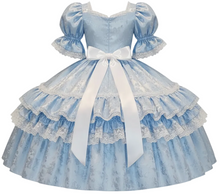 A light blue brocade satin dress with puffed sleeves, a sweetheart neckline, and a large white ribbon bow at the waist, shown on a plain white background.