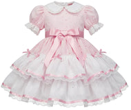 A pink and white adult baby girl's dress featuring a short puff sleeve, a white Peter Pan collar, a pink waist bow, and a tiered ruffled skirt with pink trim.
