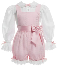 An adult baby girl's pink shortall romper with a matching pink waist bow, styled over a white long-sleeve blouse with ruffled cuffs.