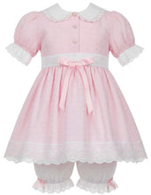 A pink baby dress with white lace trim, featuring short puff sleeves, a white Peter Pan collar, front buttons, a white waistband with a pink bow, and matching white lace-trimmed bloomers.