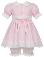 A pink baby dress with white lace trim, featuring short puff sleeves, a white Peter Pan collar, front buttons, a white waistband with a pink bow, and matching white lace-trimmed bloomers.