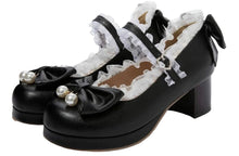 A pair of black platform Mary Jane shoes with white ruffled trim, pearl embellishments on the toes, and black bows on the sides, photographed against a plain white background.