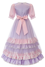 A lavender and pink tiered tulle dress with puff sleeves, a large pink bow at the waist, and white lace trim at the collar and cuffs, shown against a plain white background.